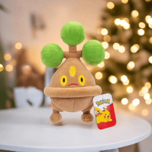Load image into Gallery viewer, Pokemon 8 Inch Plush Bonsly on display table with blurred lights in background.